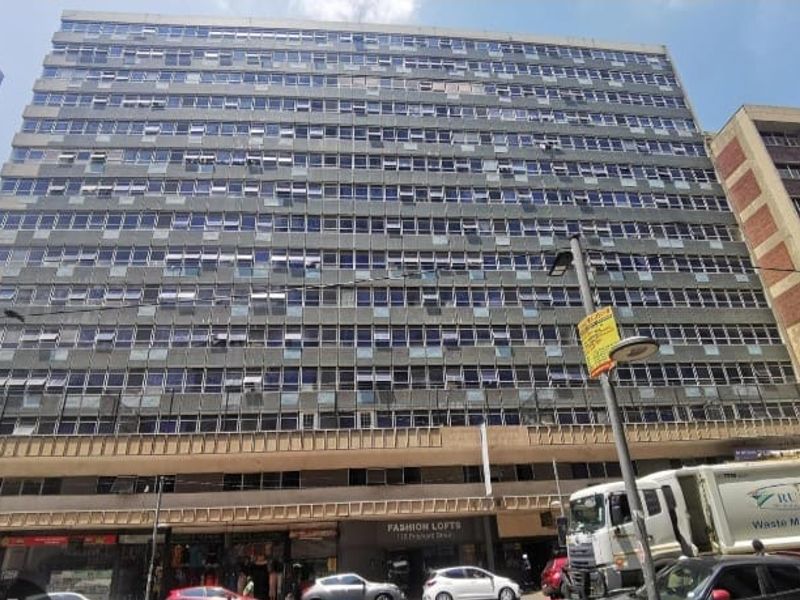 Exterior view of a multi-story apartment building featuring a large window grid and ground floor commercial space.
