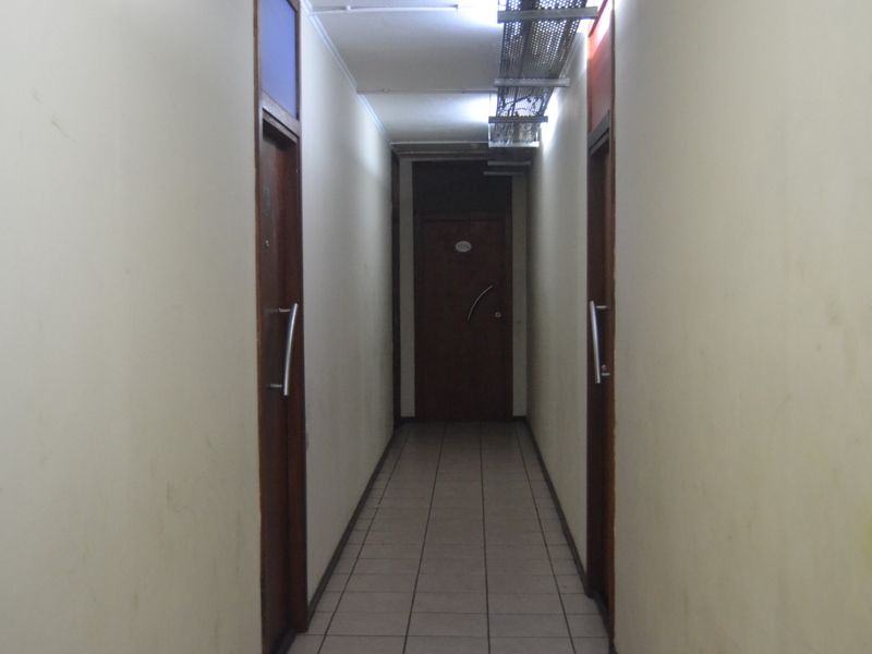 A narrow interior hallway featuring tiled flooring and multiple timber doors, showing signs of wear on the walls and exposed overhead electrical cabling.