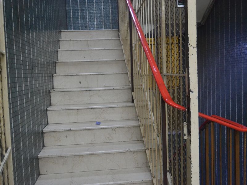 A functional apartment building stairwell featuring tiled walls, a metal balustrade, and a painted handrail.
