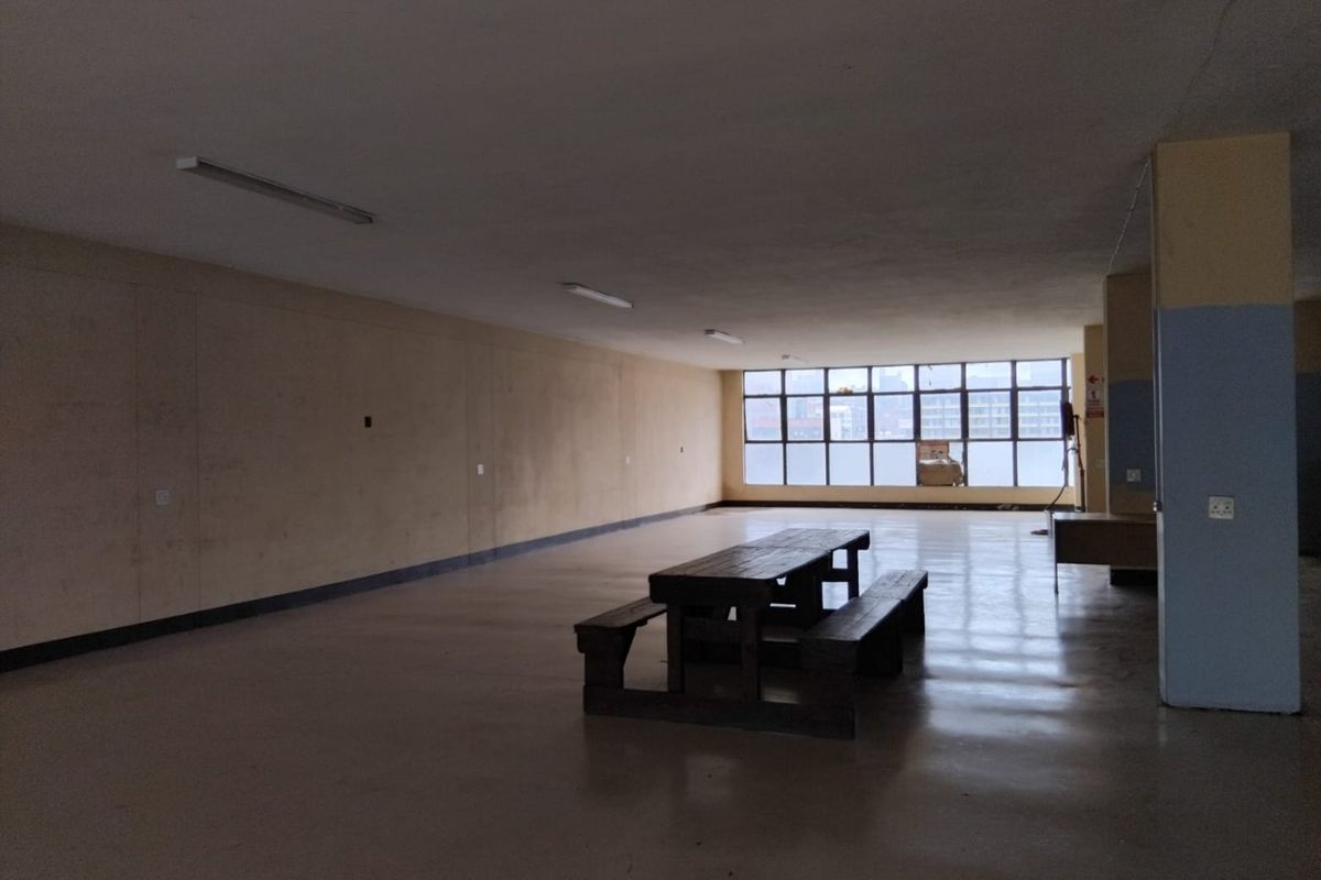 A large, open-plan commercial space featuring concrete flooring, extensive window frontage, and basic fluorescent lighting, suitable for office or retail conversion.