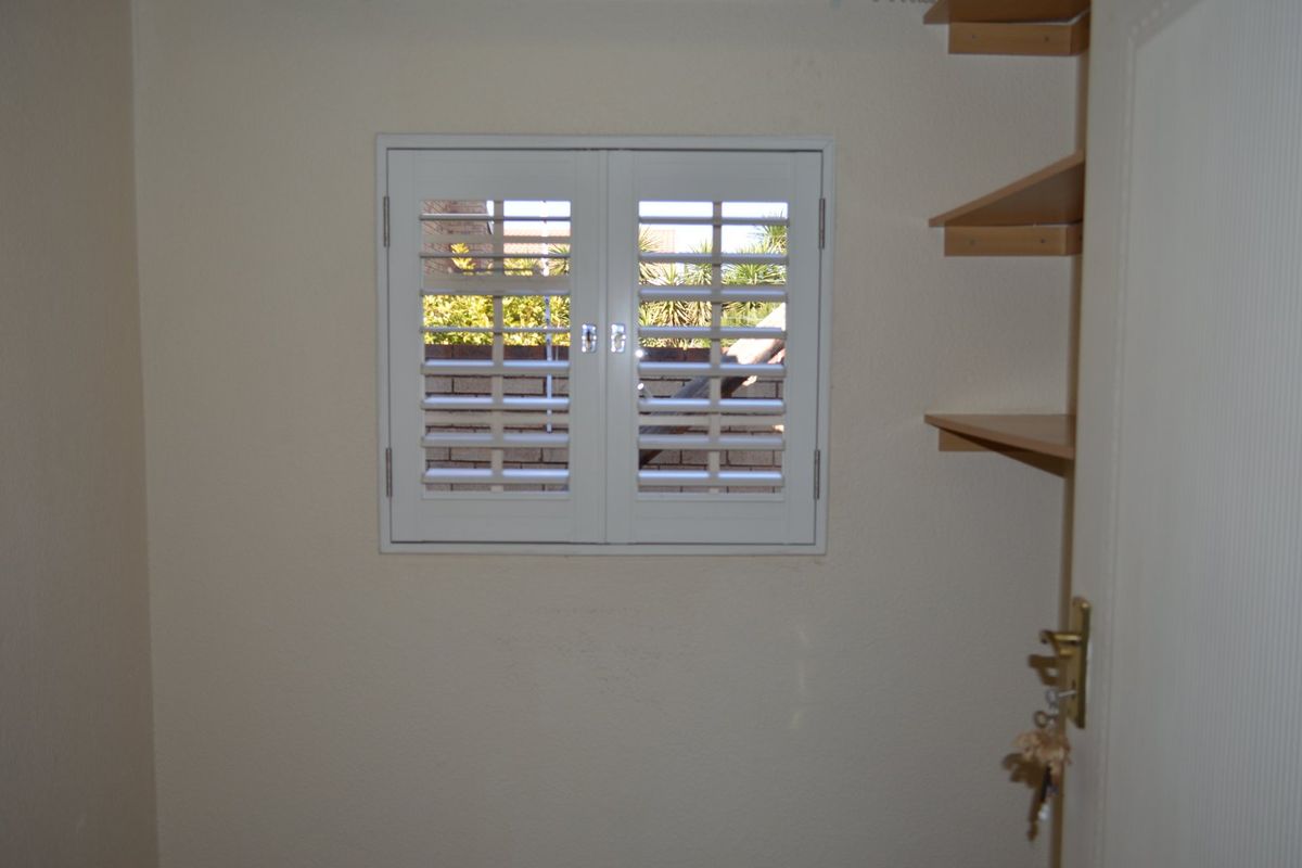 A simple room featuring white plantation shutters on the window and built-in wall shelving.