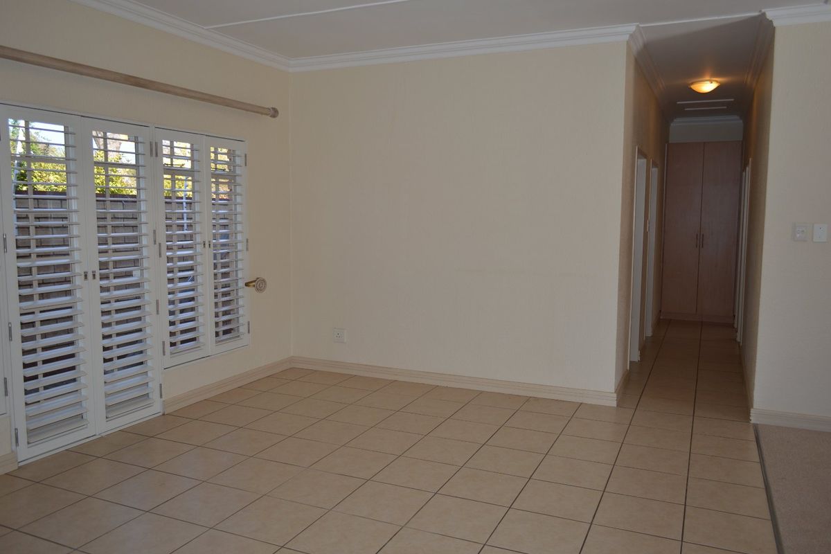 An empty living area featuring tiled flooring, plantation shutters on french doors, and access to a hallway with built-in storage.