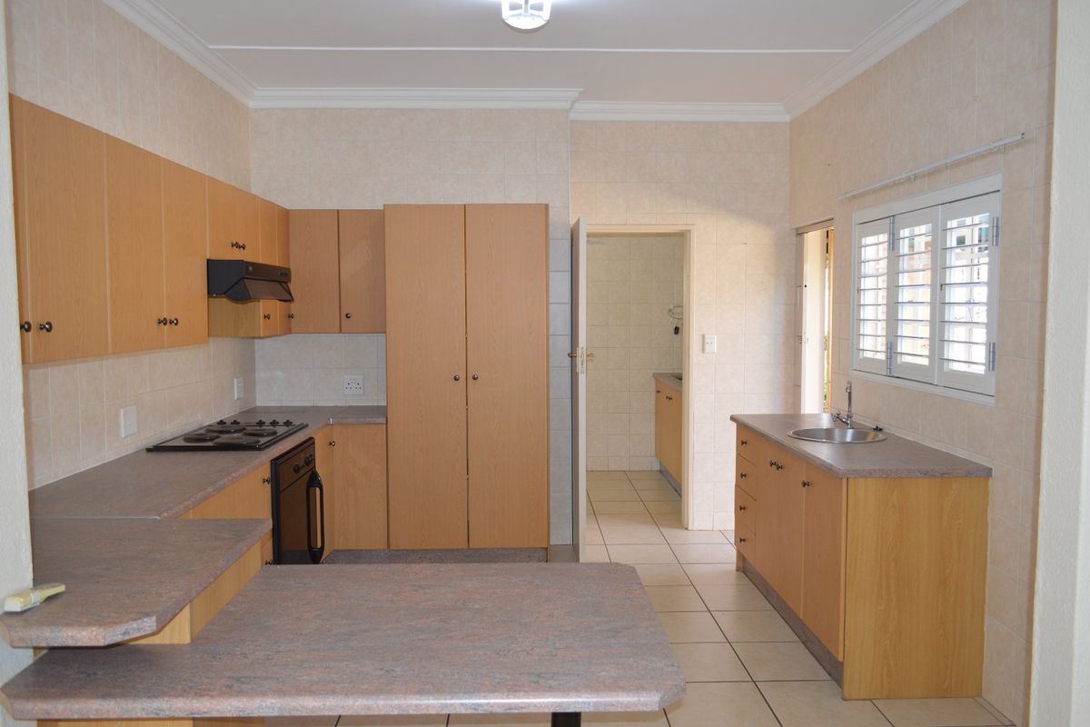 A functional kitchen featuring light wood-finish cabinetry, laminate countertops, built-in oven and hob, and tiled finishes, with an adjacent scullery area.