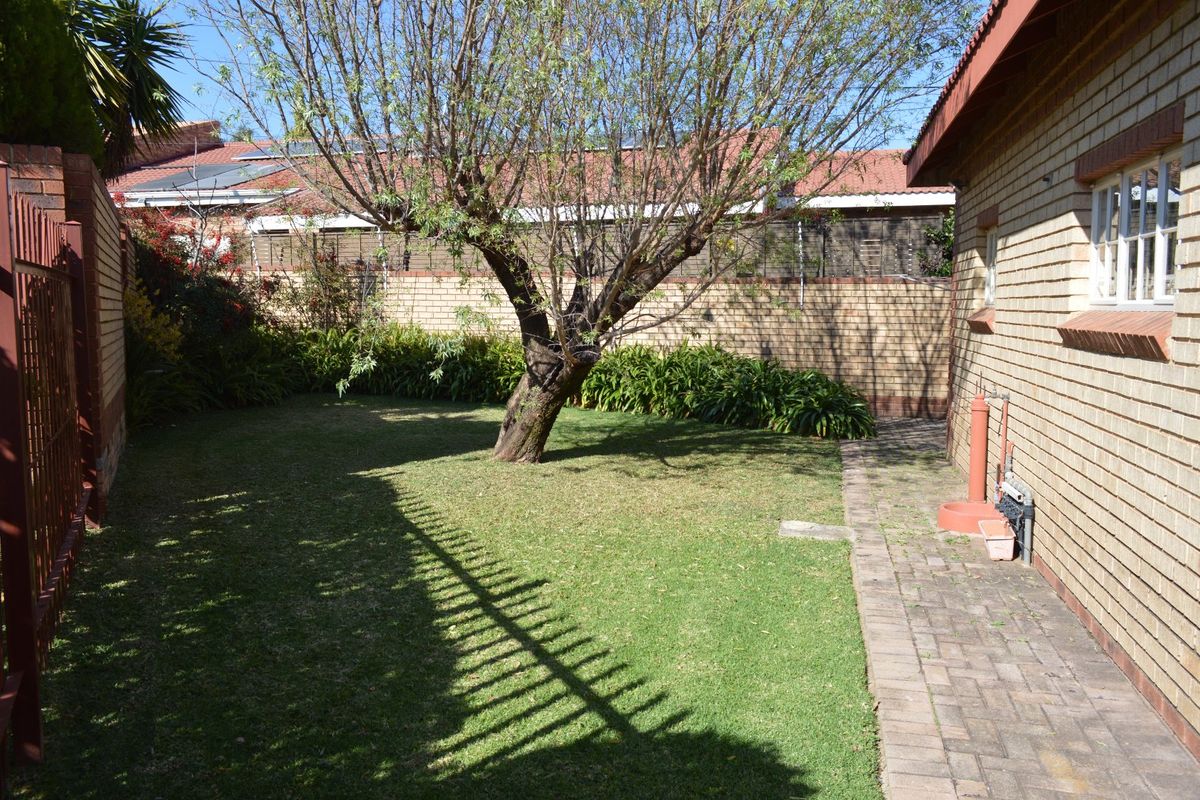 A private rear garden area featuring a well-maintained lawn, mature tree, and paved walkway alongside the facebrick exterior of the house.