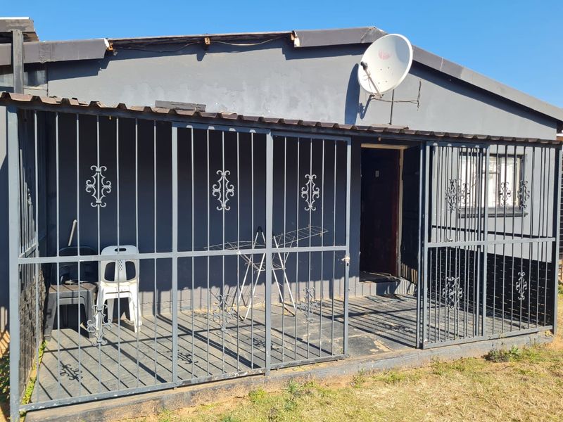 Front exterior view of a house featuring a covered patio enclosed by security gates, a satellite dish, and a corrugated metal roof.