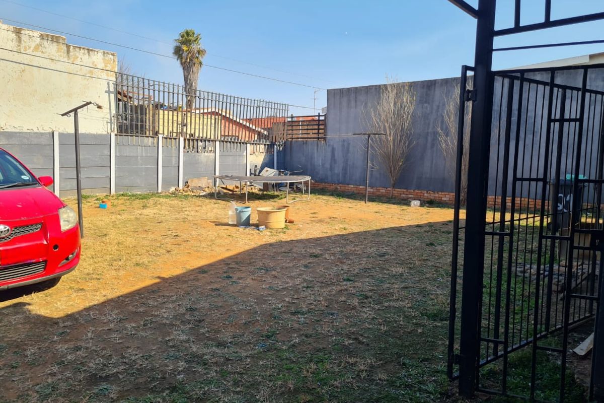 A rear garden area featuring a precast concrete boundary wall, metal security fencing, and a rotary clothesline, with a large open lawn space.