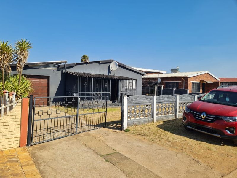 Front view of a residential property featuring a metal driveway gate, precast boundary wall, garage, and security-gated entrance.