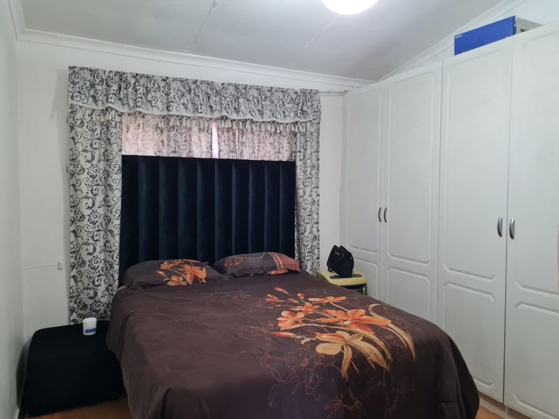 A functional bedroom featuring built-in cupboards, laminate flooring, and decorative cornicing, providing a practical space with storage solutions.