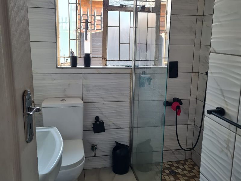 A compact bathroom featuring a walk-in shower with a rain shower head, modern wall tiling, a pedestal basin, and a toilet.