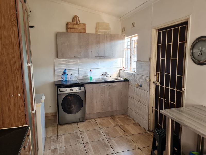 A functional laundry area featuring built-in cabinetry, a stainless steel sink, tiled backsplash, and durable floor tiles with a security gate entrance.