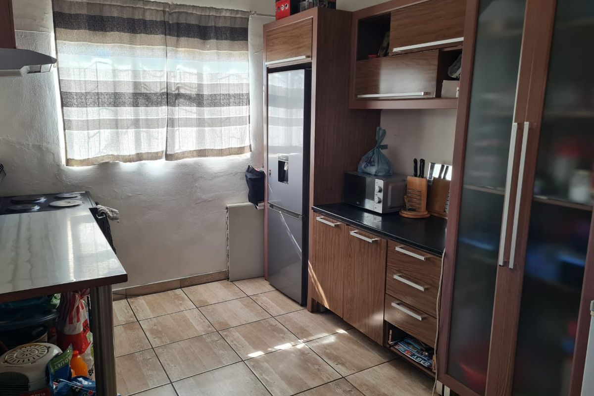 A functional kitchen featuring wood-look laminate cabinetry, dark countertops, tiled flooring, and a built-in pantry unit with glass-panel doors.
