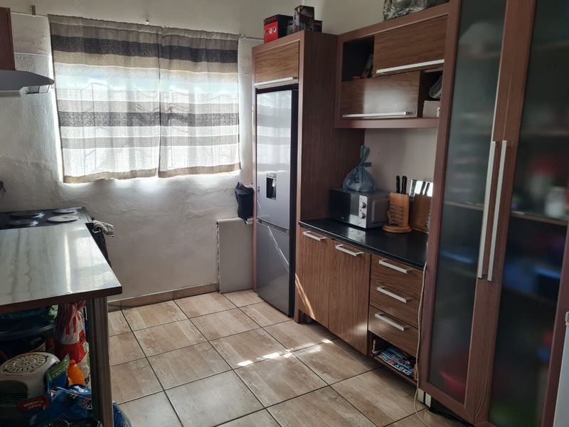 A functional kitchen featuring wood-look laminate cabinetry, dark countertops, tiled flooring, and a built-in pantry unit with glass-panel doors.