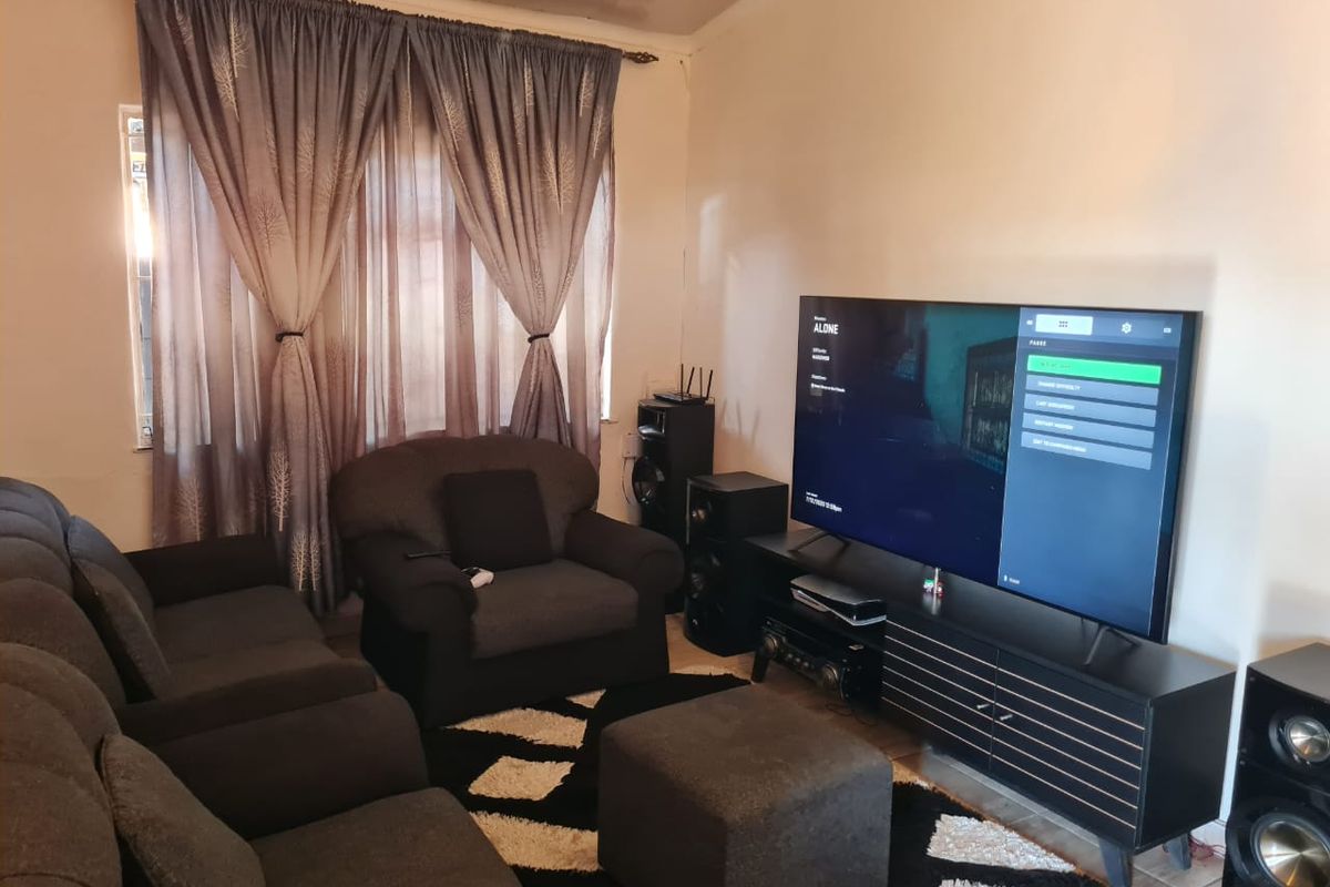 A living room featuring tiled flooring and window treatments, showing signs of ceiling wear and tear.