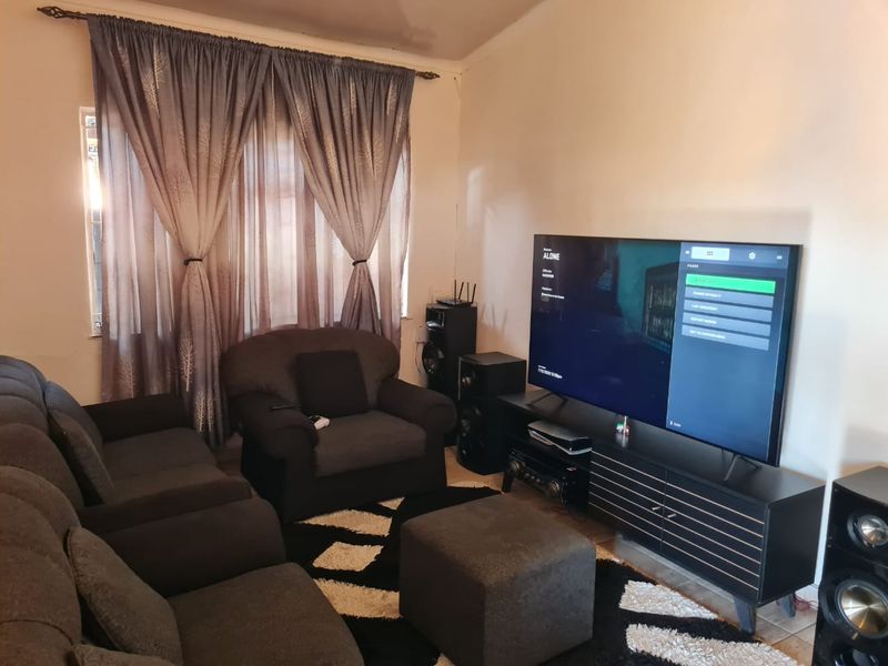 A living room featuring tiled flooring and window treatments, showing signs of ceiling wear and tear.