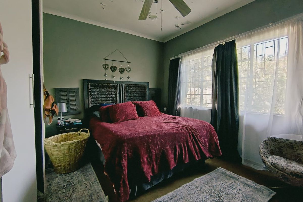 A bedroom featuring a ceiling fan and security bars on the windows, currently showing significant signs of ceiling paint deterioration.
