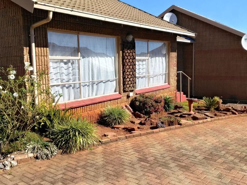 Front elevation of a brick house featuring a tiled roof, paved driveway, and established garden beds.