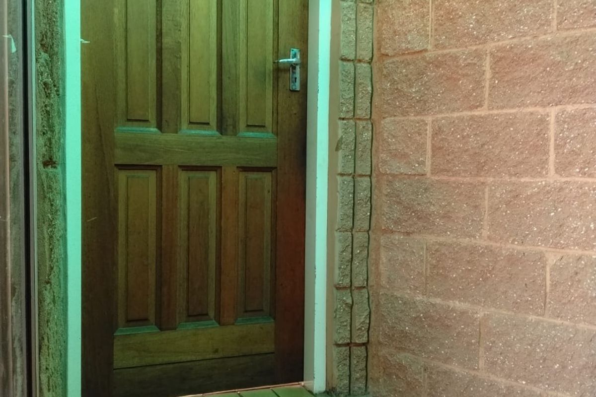 A rear exterior entrance featuring a solid timber door, brick wall construction, and tiled step area with an installed wall light.