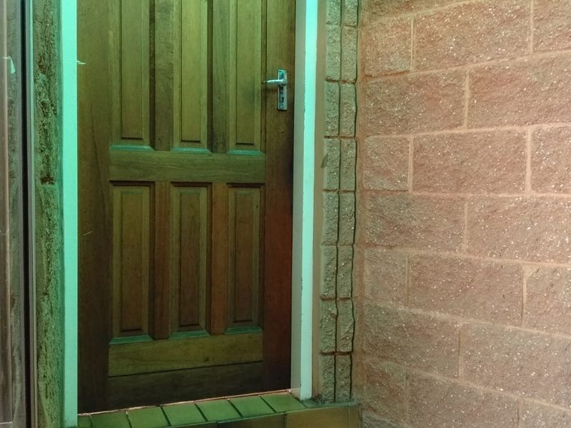 A rear exterior entrance featuring a solid timber door, brick wall construction, and tiled step area with an installed wall light.