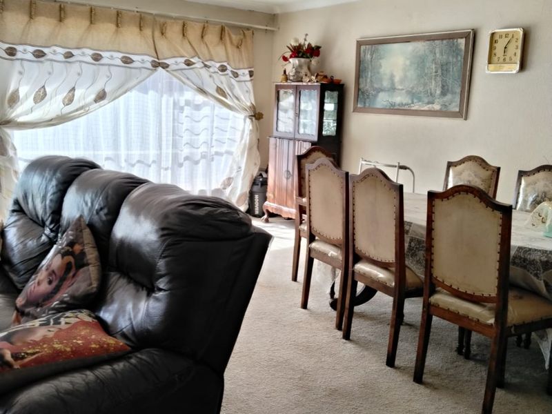 Open plan living and dining area featuring carpeted flooring and a ceiling fan, offering a functional space with potential for modernization.