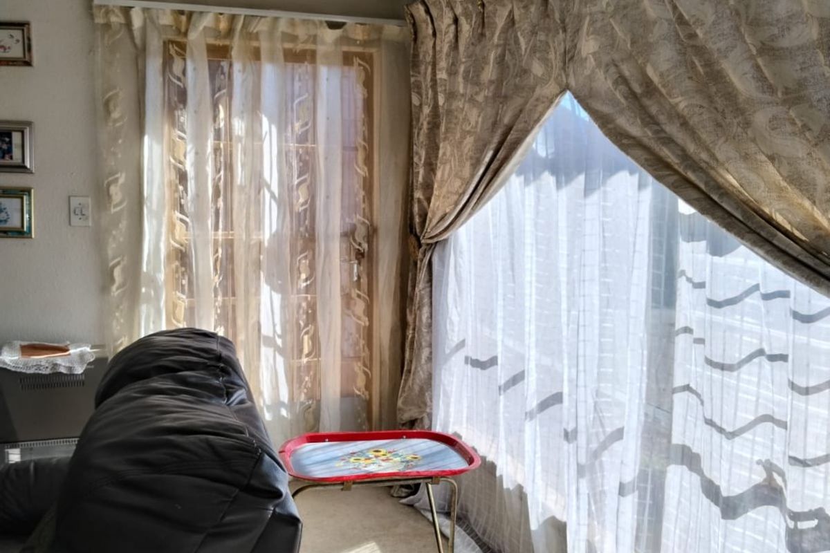 A living room area featuring large windows with curtain tracks and coving, showing signs of wear on the wall finishes.