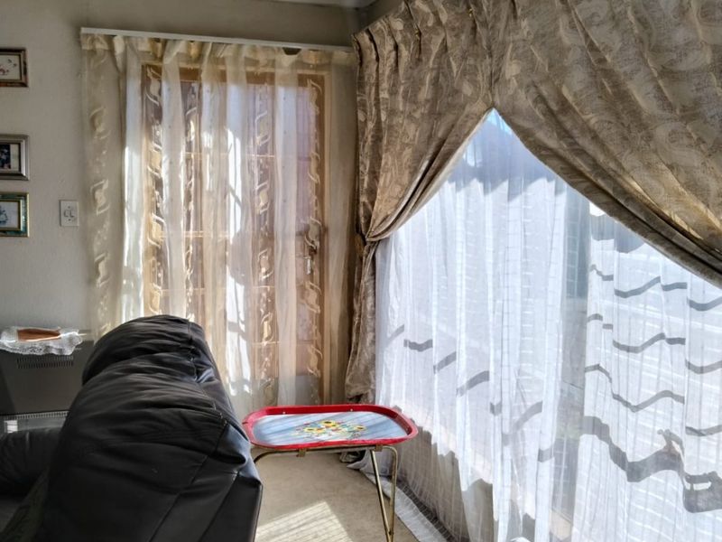 A living room area featuring large windows with curtain tracks and coving, showing signs of wear on the wall finishes.