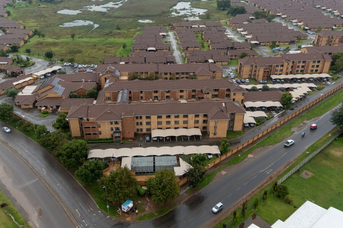 Aerial view of a residential apartment complex featuring brick buildings, tiled roofs, and covered parking areas within a landscaped estate.