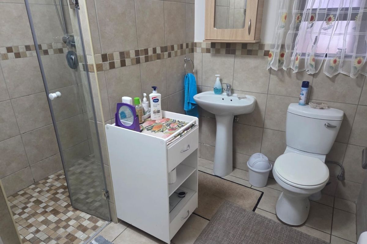 A functional bathroom featuring a pedestal basin, toilet, and a glass-enclosed shower with neutral wall and floor tiling.