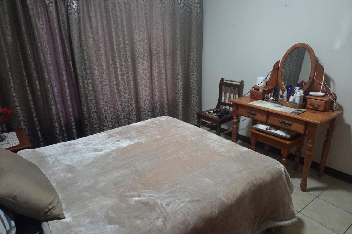 A functional bedroom featuring tiled flooring and full-length window curtains, providing a neutral base for potential interior updates.