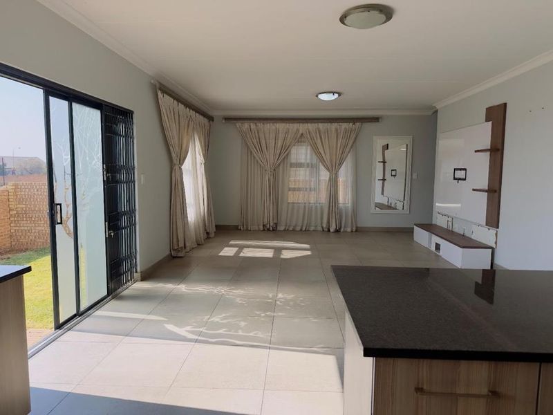 Spacious open-plan living area featuring large tiled floors, a built-in media unit, and sliding glass doors providing direct access to the garden.