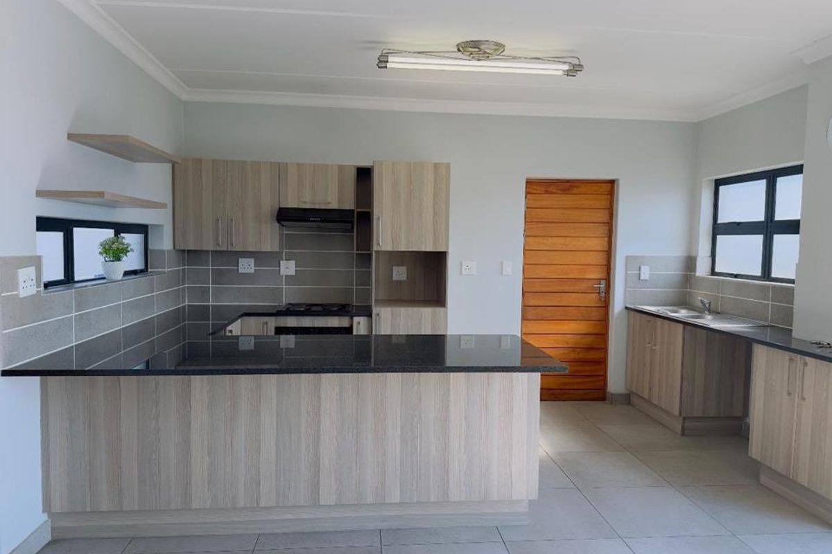Modern kitchen featuring light wood-grain cabinetry, dark granite countertops, a gas hob with extractor, and tiled splashbacks in a clean, open-plan layout.