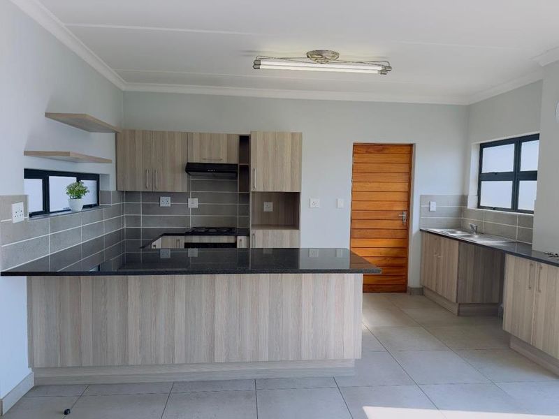 Modern kitchen featuring light wood-grain cabinetry, dark granite countertops, a gas hob with extractor, and tiled splashbacks in a clean, open-plan layout.