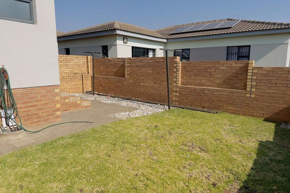 A rear garden area featuring a brick boundary wall, paved patio section, and lawn, offering potential for landscaping and outdoor living development.