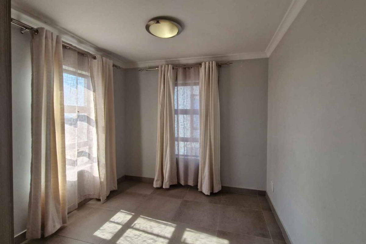 A bright, empty bedroom featuring neutral tiled flooring, coved ceilings, and dual windows with curtain rods.