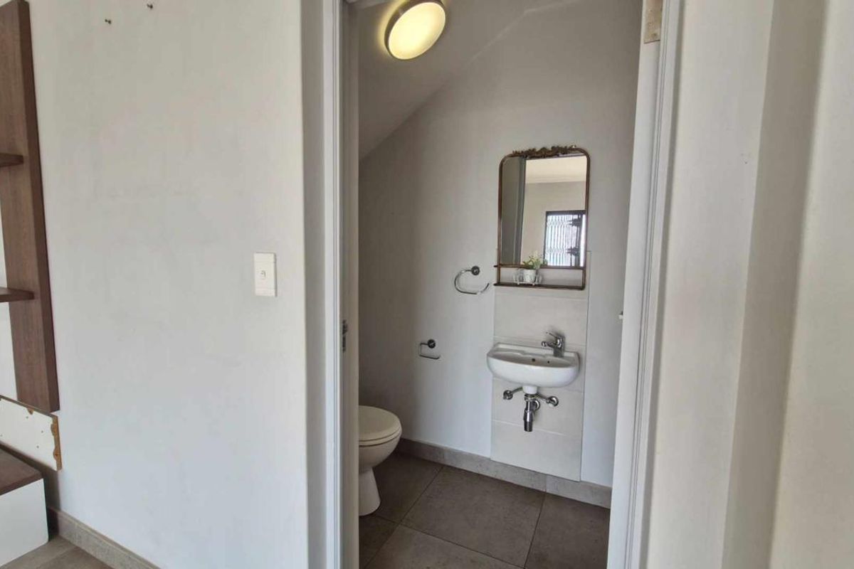 A compact guest bathroom featuring a wall-mounted basin, toilet, and tiled flooring, presenting a functional space in need of minor cosmetic updates.