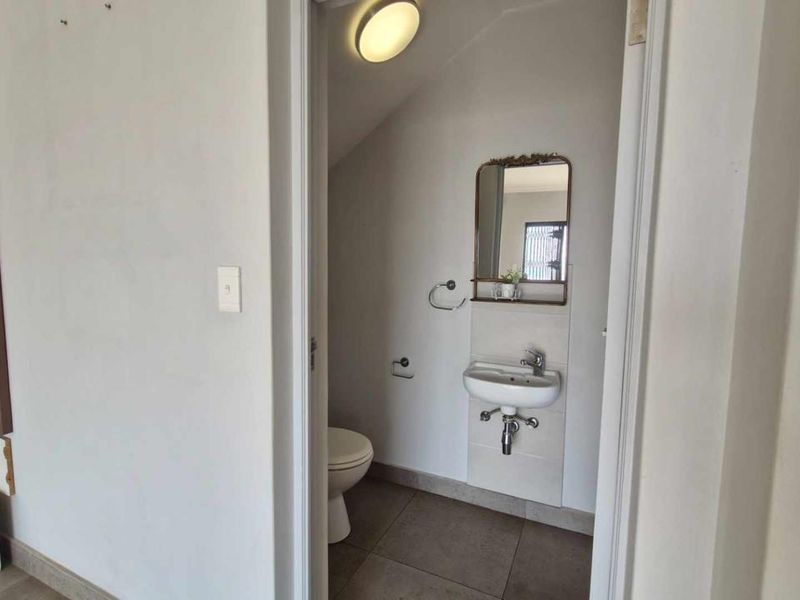 A compact guest bathroom featuring a wall-mounted basin, toilet, and tiled flooring, presenting a functional space in need of minor cosmetic updates.
