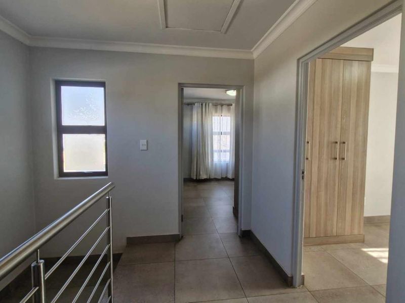 A bright, tiled hallway featuring a modern stainless steel balustrade and access to adjacent rooms with built-in storage.