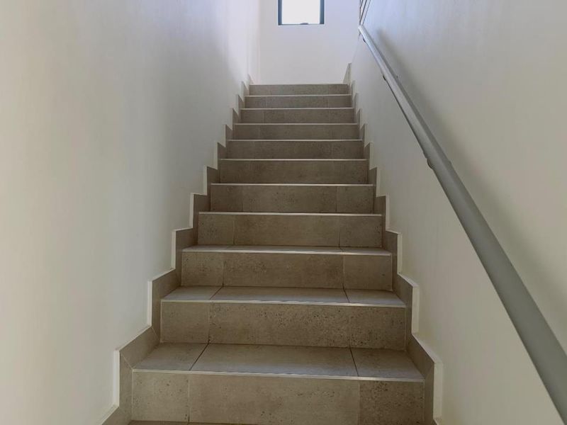 A clean, modern staircase featuring neutral-toned floor tiles and a simple handrail, leading to an upper level.