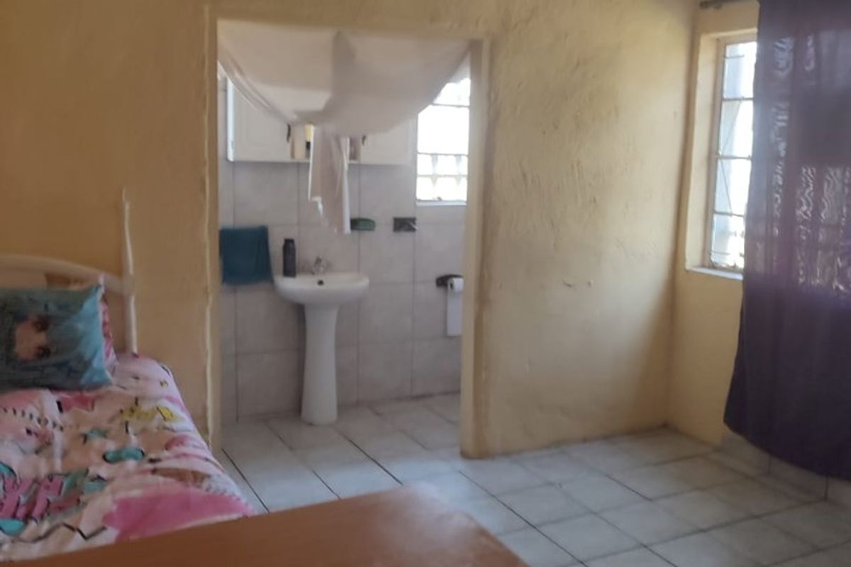 A bedroom featuring tiled flooring and an en-suite bathroom with a pedestal basin, requiring cosmetic updates to the walls and ceiling.