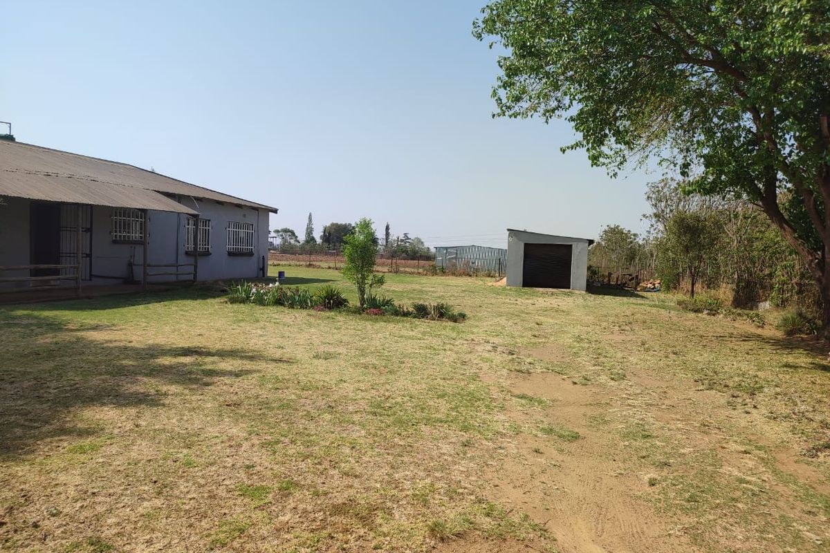 Spacious rear garden area featuring a detached garage, established trees, and a view of the main dwelling with security bars.