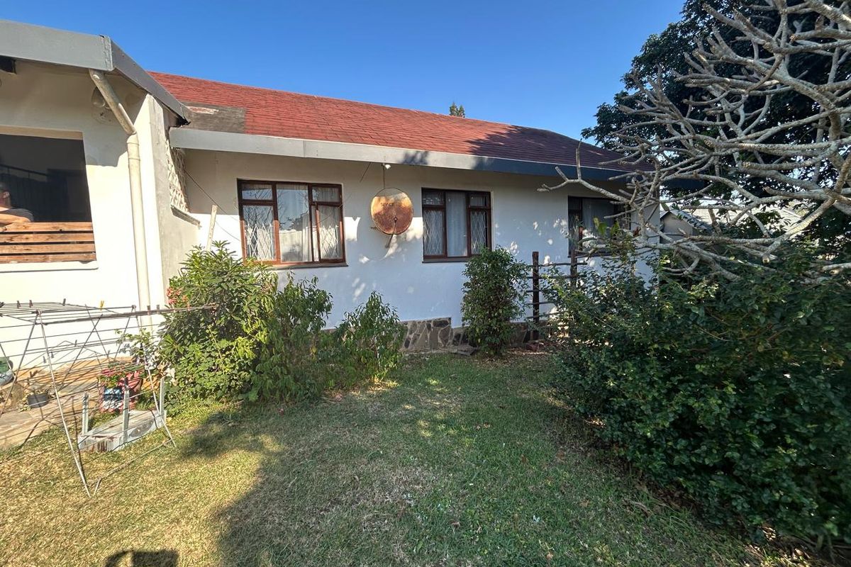 Rear view of the house showing a tiled roof, metal window frames with security bars, and a small garden area.