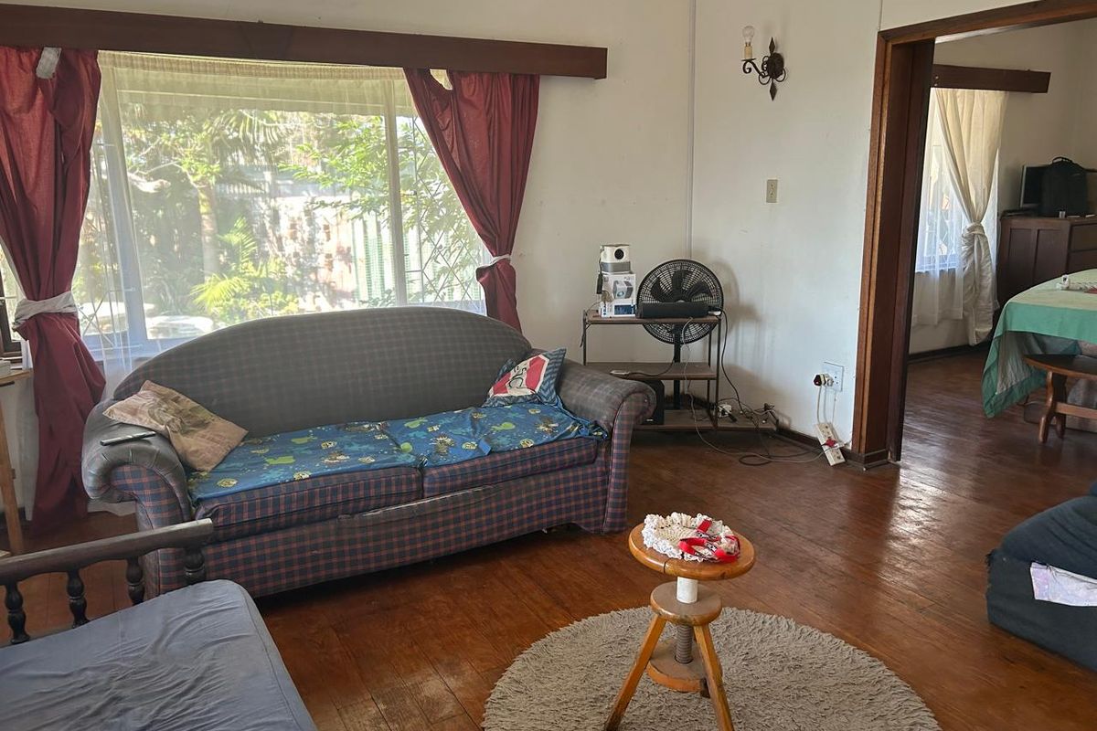 A living room featuring original timber flooring and large windows, offering a dated interior space with potential for modernization and cosmetic updates.
