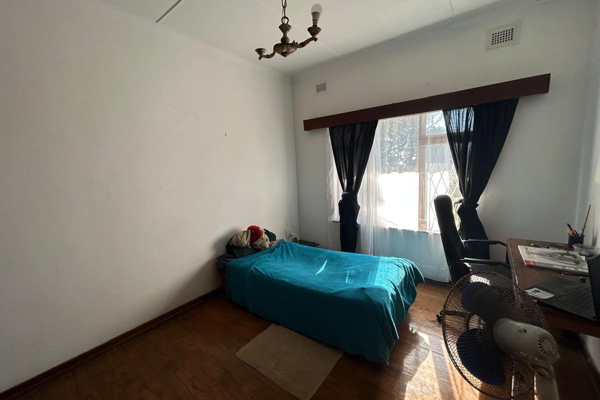 A bedroom featuring timber flooring, a central light fixture, and natural light through a window with a wooden pelmet.