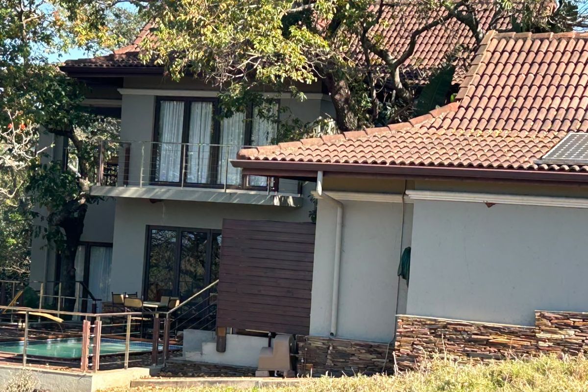 Rear view of a multi-story house featuring a swimming pool, upper-level balcony, stone cladding accents, and traditional terracotta roof tiles.