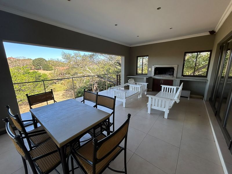Spacious covered patio featuring a built-in braai, stone prep surfaces, and a glass balustrade overlooking the surrounding landscape.