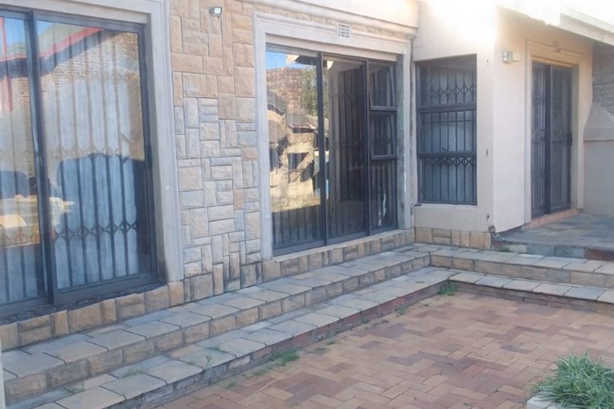 Rear exterior view featuring a paved patio area, stone-clad facade, and multiple sliding glass doors with security gates.