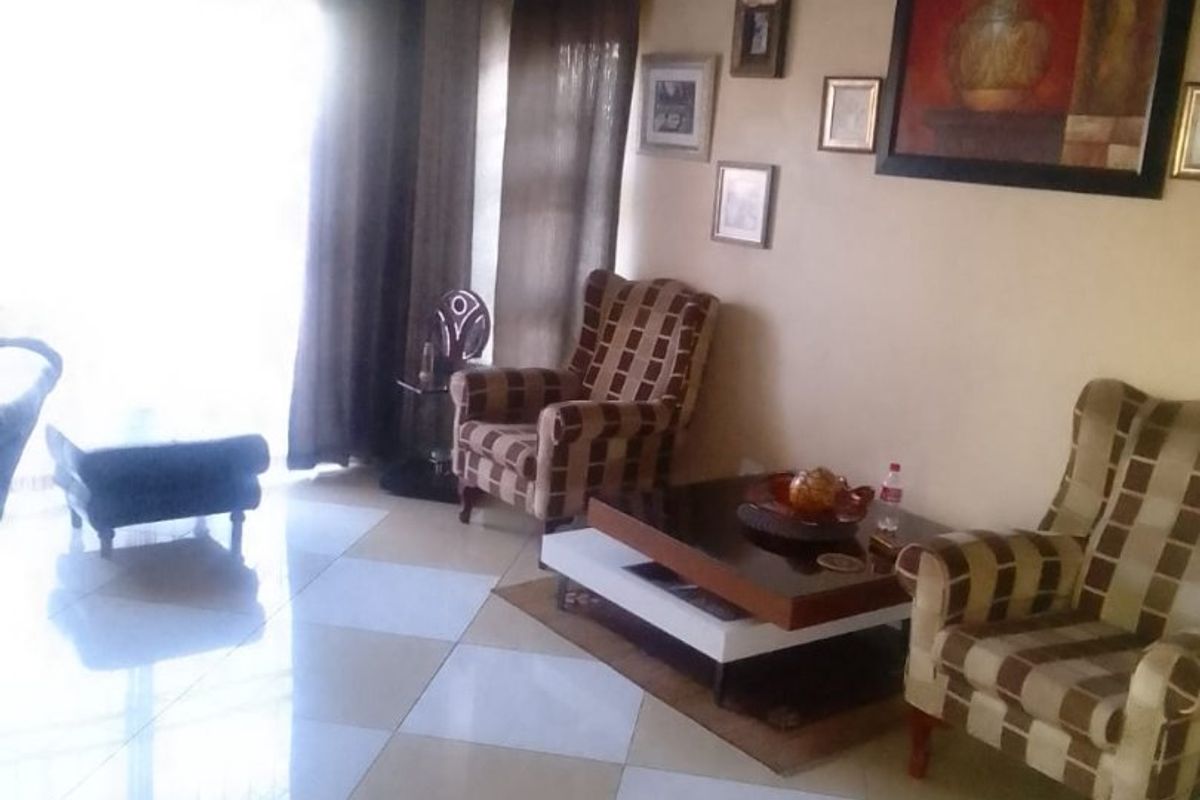 A living room featuring large format checkered floor tiles and a drop ceiling, offering a functional space with natural light from the adjacent window.
