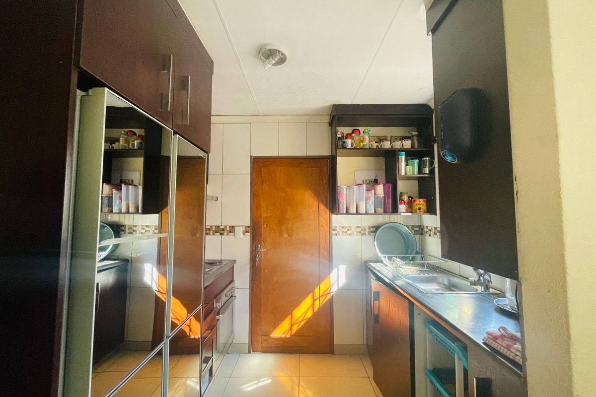 A functional kitchen featuring dark built-in cabinetry, tiled backsplash, stainless steel sink, and tiled flooring with direct access to an adjacent room.
