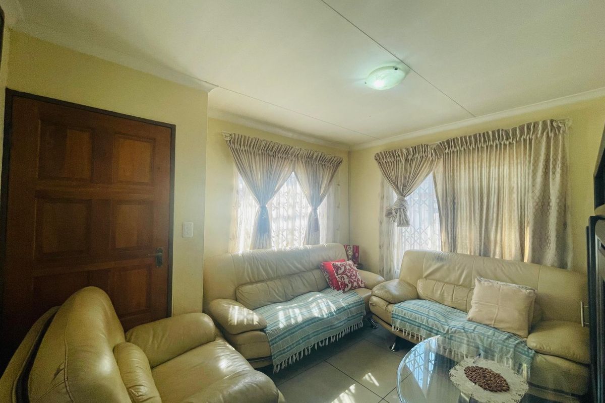 A living room featuring tiled flooring, natural light through windows with security gates, and a timber door.