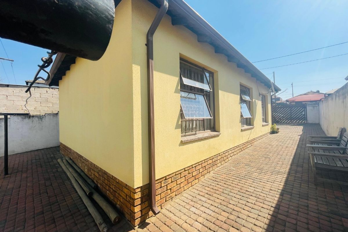 Rear exterior view of the property featuring yellow rendered walls, brick plinth detailing, and paved outdoor area.