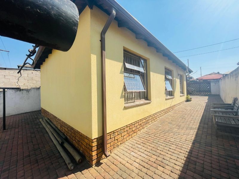 Rear exterior view of the property featuring yellow rendered walls, brick plinth detailing, and paved outdoor area.